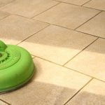 Green and steel tile cleaning machine standing on beige tiles showing freshly cleaned tiles